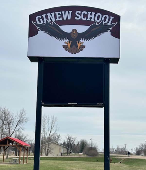 Digital messaging board along the roadside at the Ginew School at Roseau River Anishinabe First Nation. The sign shows the Ginew School logo (an eagle) above the digital sign.
